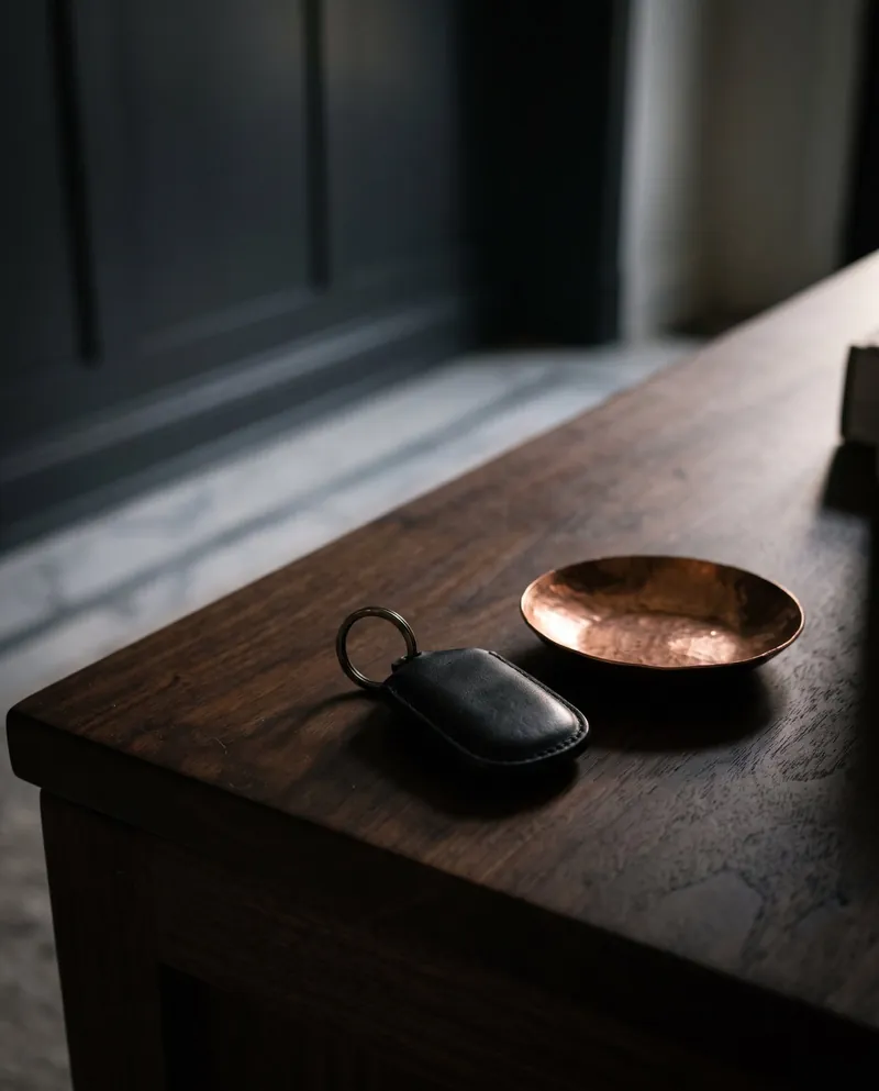 A leather key fob beside a small copper dish on a polished walnut table.